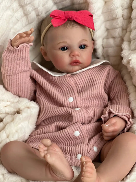 Reborn baby doll close up with raised hand and red bow headband