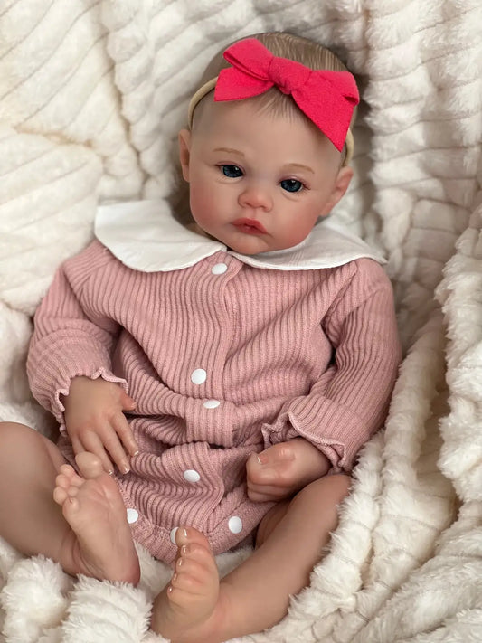 Reborn baby doll lying on knit blanket wearing pink romper and red bow