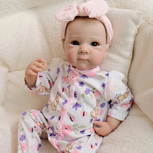 Reborn baby doll lying on cream blanket in floral bunny romper