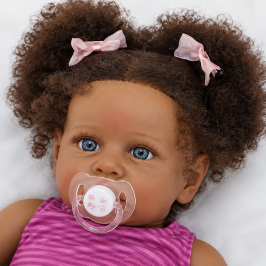 Close up of reborn toddler doll face with hand-rooted curly hair puffs, pink bows, blue eyes and pacifier