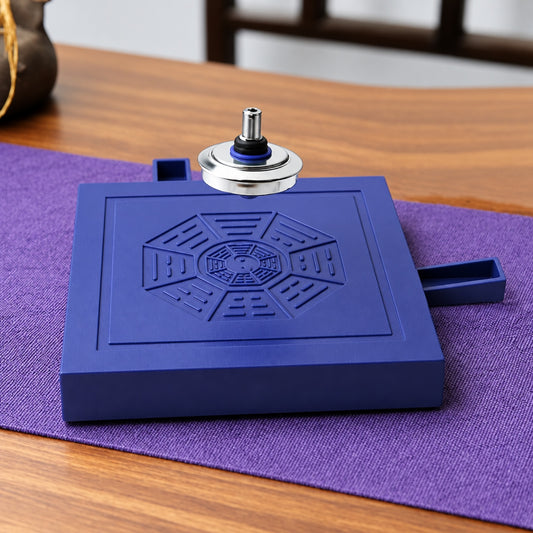 Silver magnetic spinning top floating above a blue square levitation base with embossed octagonal pattern on a wooden desk